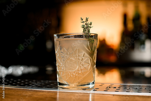Close-up view of glass with cocktail garnished with rosemary on blurred background
