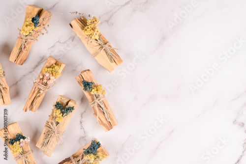 Holy wood sticks for yoga, meditation and spiritual practices. Palo santo sticks decorated with dried flowers over white marble table background with copy space for text
