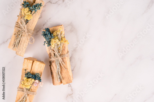 Holy wood sticks for yoga practice, meditation and spiritual practices. Palo santo sticks with dried flowers over white marble table background with copy space for text