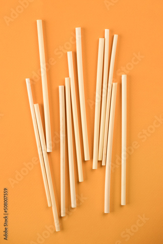 Natural wheat drinking straws made of the stem of the wheat plant on orange background. Sustainable lifestyle and zero waste concept. Ethical consumerism. Flat lay
