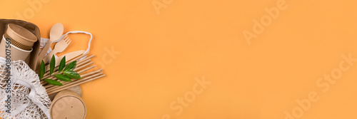 Banner with paper food cups, containers, wooden cutlery set and drinking straws in white cotton net bag on orange background with copy space. Street food take away paper utensils
