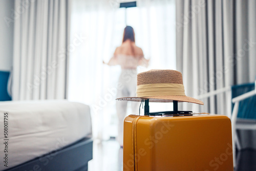 Stampa su tela Close-up luggage with hat and blurred happy tourist woman background in hotel after check-in