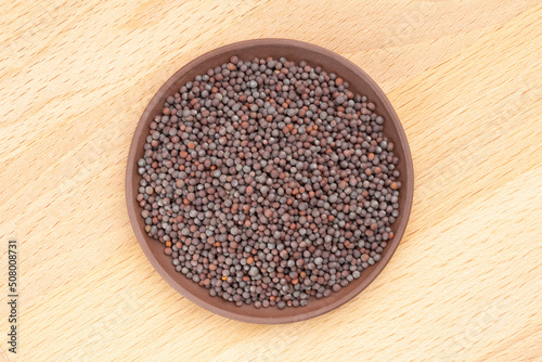 Spice Mustard seeds (Brassica juncea) in brown clay plate on yellow wooden background. Close up. Healthy diet concept