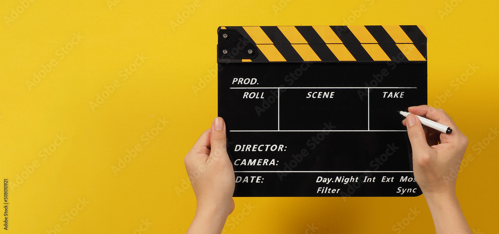  The hands are holding a black with yellow clapper board and marker Pen on white background..