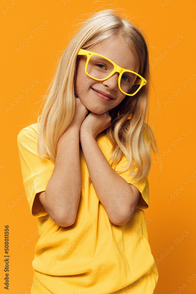 a cute, funny girl, of school age, stands on a yellow background in a yellow T-shirt in yellow glasses, posing funny. Horizontal studio photography with blank space for advertising mockup a cute, funny girl, of school age, stands on a yellow background in a yellow T-shirt in yellow glasses, posing funny. Horizontal studio photography with blank space for advertising mockup