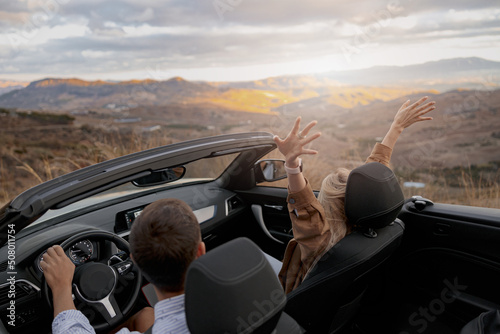 Photo Rear of couple man and woman traveling in convertible car by mountainside enjoyi