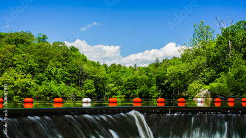 Fotografering Buoys near dam edge in beautiful spring day with green trees and blue sky