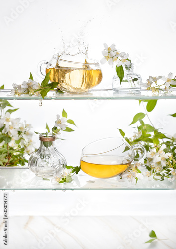 Jasmine tea on a glass shelf .Two transparent cups with green tea and white flowers .