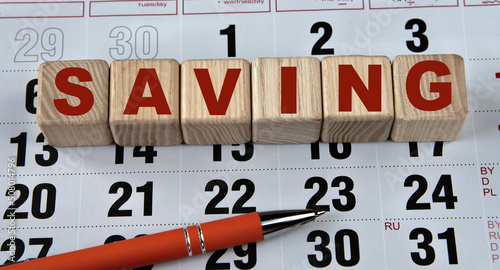 SAVING - word on wooden cubes on the background of the calendar and pen