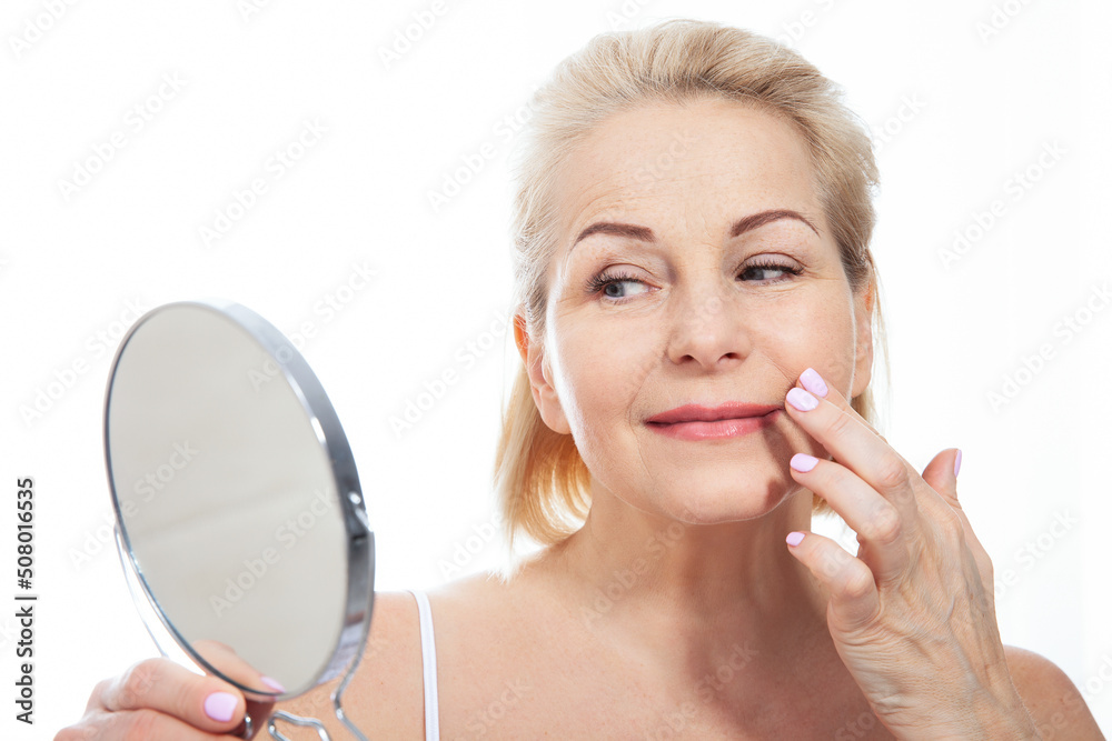 Happy middle aged woman model touching face skin looking in mirror. Smiling mature older lady enjoying healthy skin care, aging beauty, skincare treatment cosmetic products concept. Happy middle aged woman model touching face skin looking in mirror. Smiling mature older lady enjoying healthy skin care, aging beauty, skincare treatment cosmetic products concept.