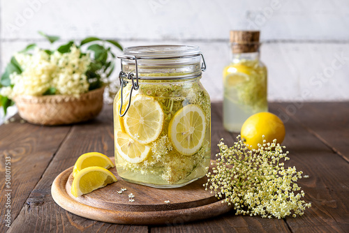 Elderberry infused water or syrup made with fresh flowers and lemons as basic ingredients. Wooden background