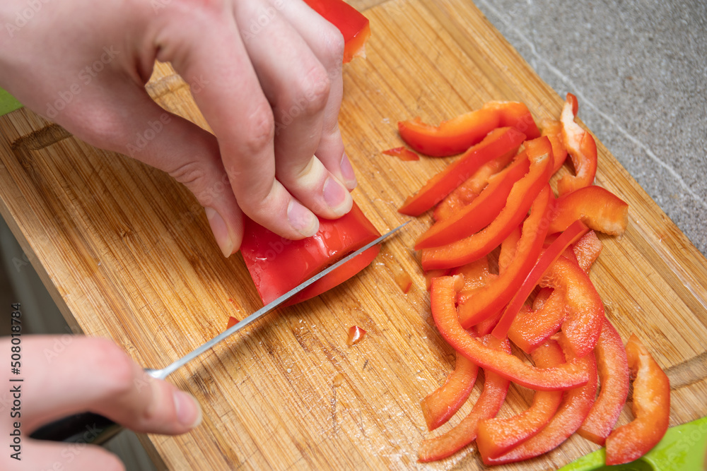 Female hands slicing red juicy raw peppers on a board, close-up. The concept of cooking homemade food. Preparing salad in the kitchen. Diet food concept Female hands slicing red juicy raw peppers on a board, close-up. The concept of cooking homemade food. Preparing salad in the kitchen. Diet food concept