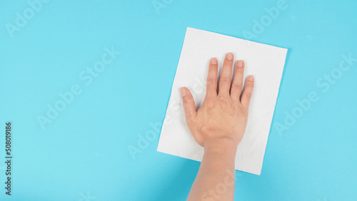 Hand is wiping and hold white paper tissue on blue background. Empty space for text . Top down view.