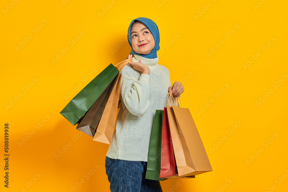 Cheerful beautiful Asian woman in white sweater showing so many shopping bags, shopping discount promo isolated over yellow background