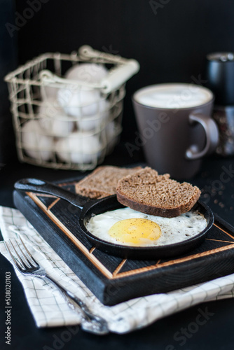 fried eggs on a cast-iron frying pan with black bread on a dark background
