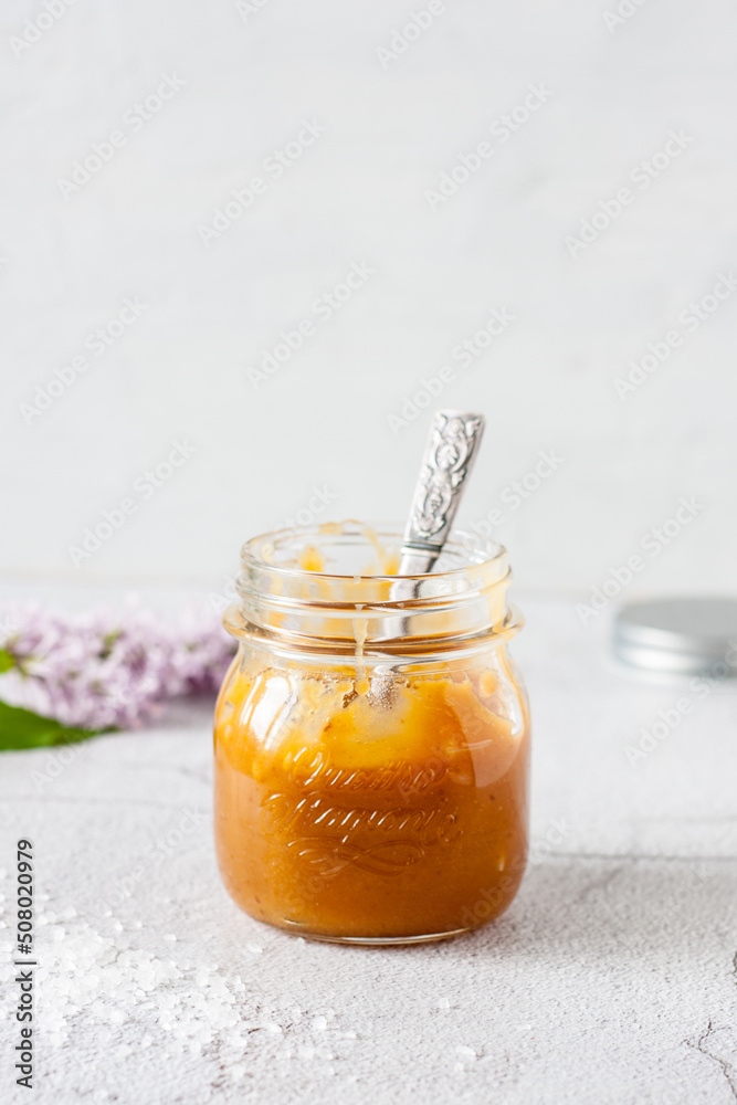caramel sauce in a glass jar with a spoon inside on a light background caramel sauce in a glass jar with a spoon inside on a light background