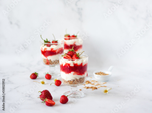 Foto Italian strawberry tiramisu dessert with mascarpone and whipped cream, savoyardi crumb and fresh strawberry in glass on marble
