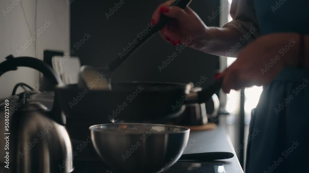 woman is frying pancakes for breakfast, housewife is pouring dough on frying pan, standing near stove woman is frying pancakes for breakfast, housewife is pouring dough on frying pan, standing near stove