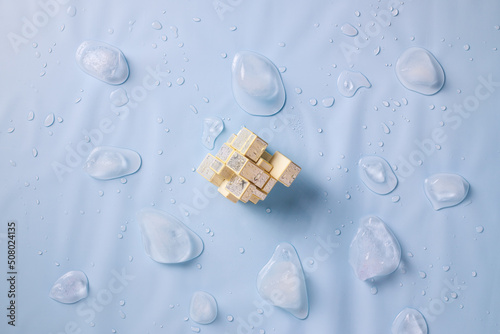 Foto Golden mirror rubik's cube, pieces of melted ice on a blue background with water drops