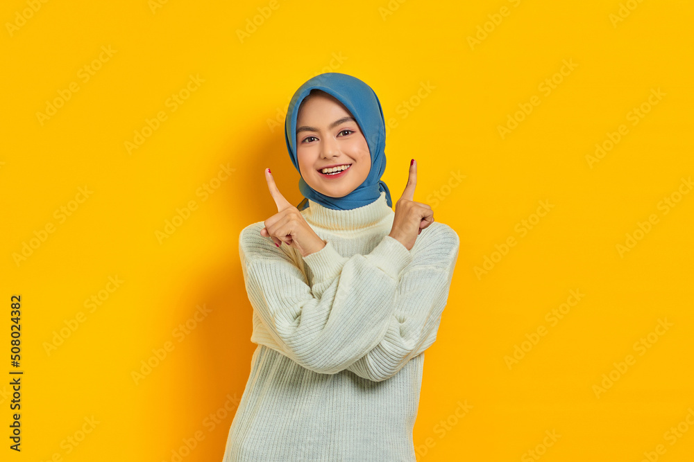 Cheerful young Asian woman in white sweater pointing finger up at copy space isolated over yellow background Cheerful young Asian woman in white sweater pointing finger up at copy space isolated over yellow background