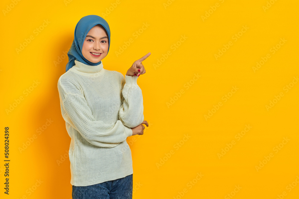 Beautiful Asian woman in white sweater pointing fingers aside at copy space isolated over yellow background Beautiful Asian woman in white sweater pointing fingers aside at copy space isolated over yellow background