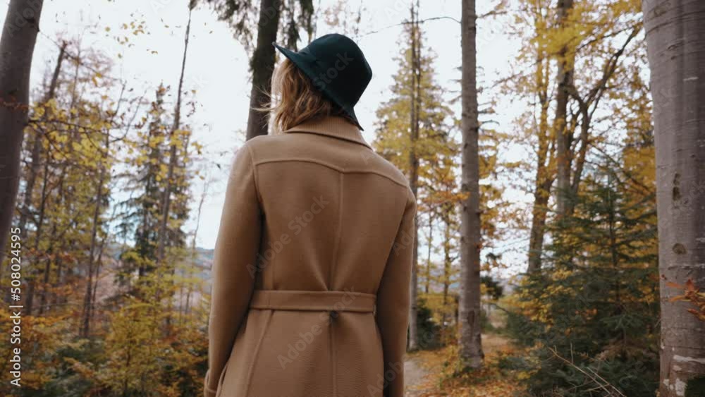 Girl walks through woods between trees and looks around and enjoys nature. Fallen yellow leaves in park. Autumn time. Walk in fresh air. Woman walks in woods with tall trees.Peace and energy in nature Girl walks through woods between trees and looks around and enjoys nature. Fallen yellow leaves in park. Autumn time. Walk in fresh air. Woman walks in woods with tall trees.Peace and energy in nature