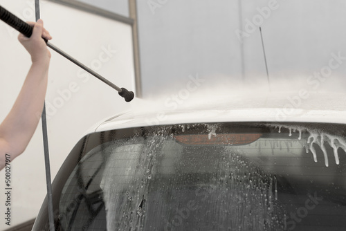 Close-up of a woman's hand holding a pressure washer hose cleaning a white car.