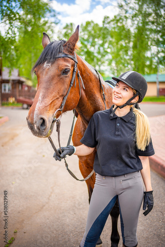 Lovely young woman wearing helmet stroking to her brown horse © dtatiana