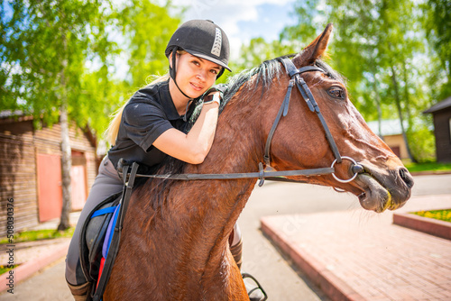 Lovely young woman wearing helmet riding her brown horse