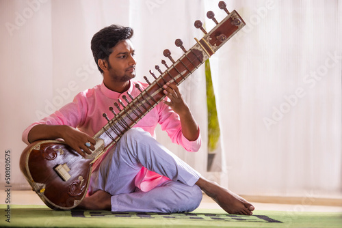 Young male musician playing Sitar at home photo