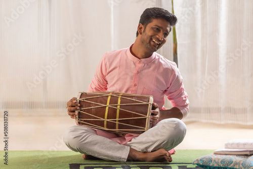 Portrait of young man playing Dholak at home photo