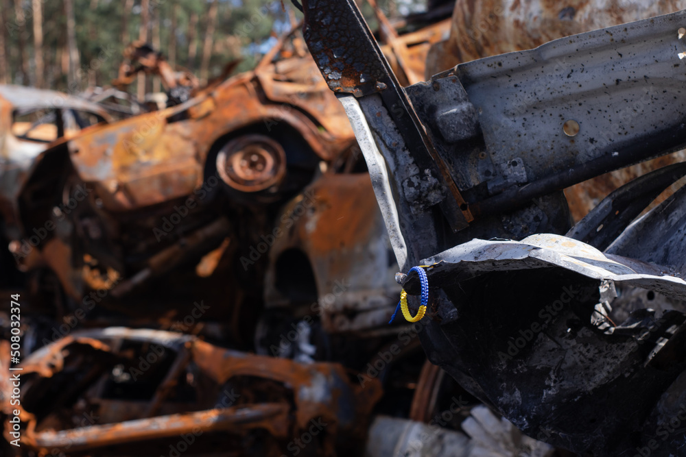 bracelet as symbol of ukraine - flag from blue and yellow with burnt out cars on background from russian attack. russian military war crimes against ukraine. glory to ukraine