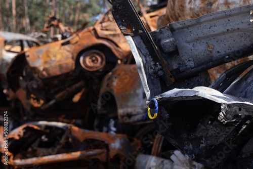 bracelet as symbol of ukraine - flag from blue and yellow with burnt out cars on background from russian attack. russian military war crimes against ukraine. glory to ukraine