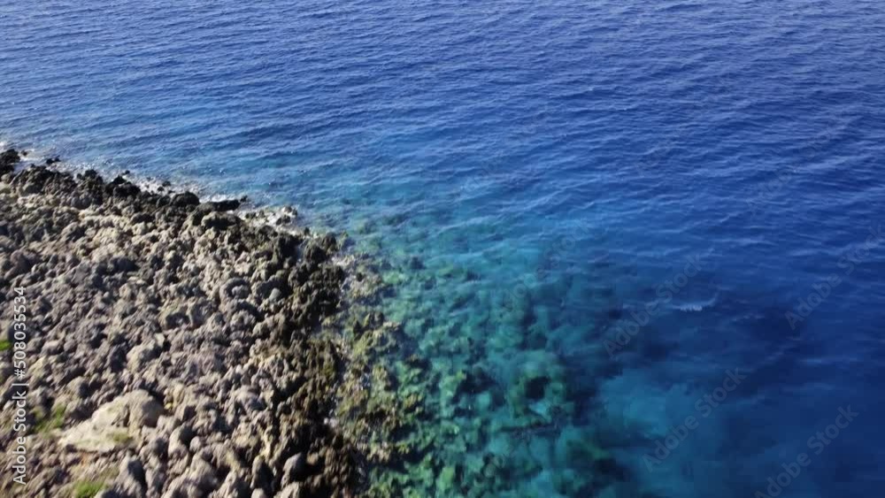 Landscape of the sea with reef bottom and transparent water next to rocky coast filmed by drone. Aerial view on the blue ocean with mountain range on backdround at clear summer day. Concept of nature. Landscape of the sea with reef bottom and transparent water next to rocky coast filmed by drone. Aerial view on the blue ocean with mountain range on backdround at clear summer day. Concept of nature.