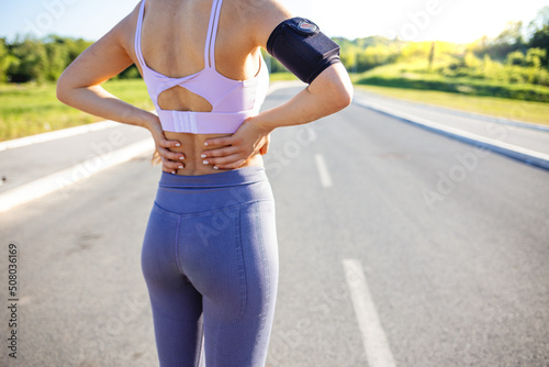 Young woman with an athletic figure and a lower back injury. Back pain during sports. Cropped shot of an unrecognizable woman standing alone outside and suffering from backache during her run.