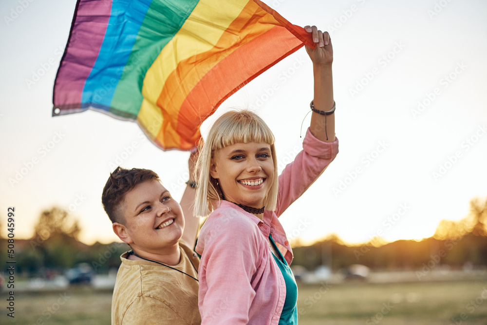 Young lesbians have fun with rainbow flag in nature and looking at camera. Young lesbians have fun with rainbow flag in nature and looking at camera.