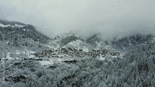 Snowy winter village in a valley surrounded by forests and mountains covered in clouds. French Alps scenery near La Plagne and Les Arcs in Champagny en Vanoise. photo