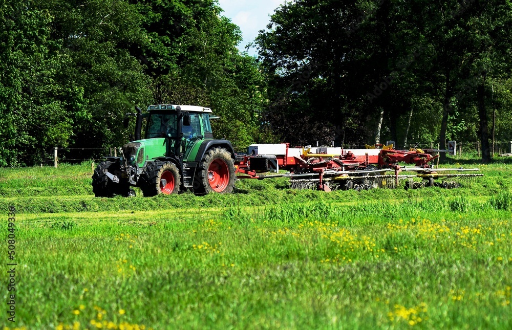 Tractor with tedder in may under blue sky Tractor with tedder in may under blue sky