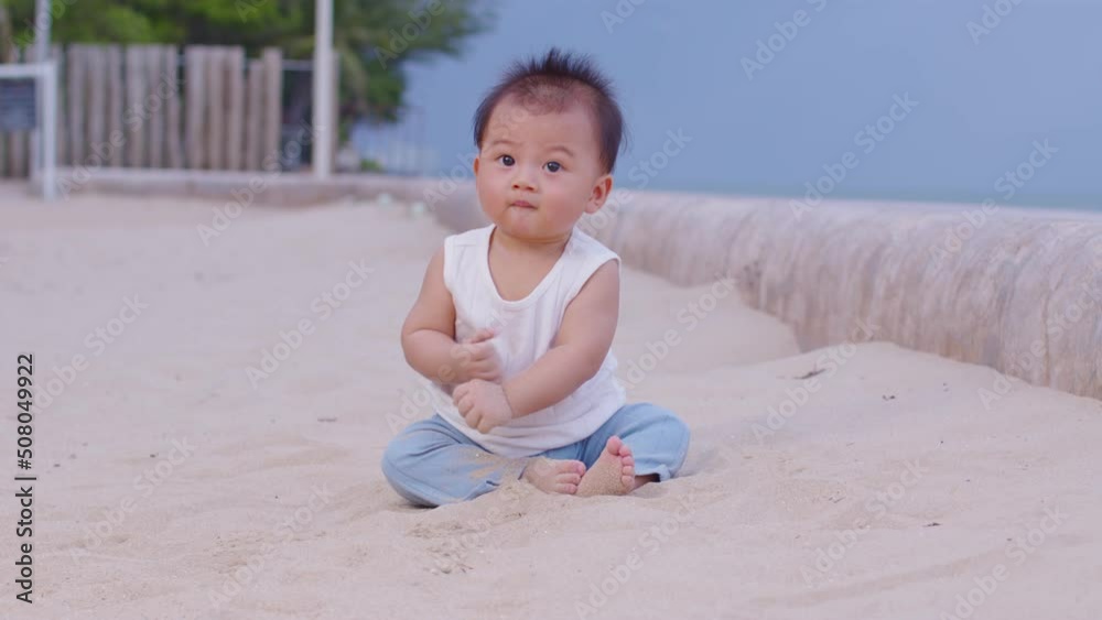 Adorable asian baby sit on sand spend time to learn all around beach and sea. First time to touch sand of cute baby infant excite and happiness. Little baby boy playing outdoor and looking at camera Adorable asian baby sit on sand spend time to learn all around beach and sea. First time to touch sand of cute baby infant excite and happiness. Little baby boy playing outdoor and looking at camera