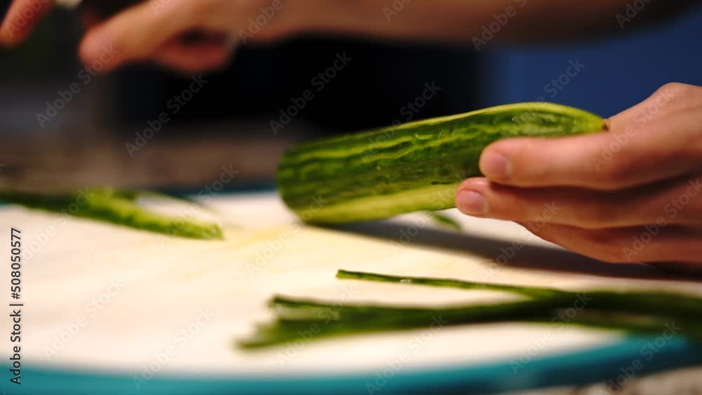 Slowly peeling healthy cucumber with vegetable scraper in home kitchen, close-up Slowly peeling healthy cucumber with vegetable scraper in home kitchen, close-up