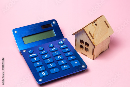 Wooden house and calculator on a pink background. Real estate purchase and sale concept. Real estate services. Home insurance