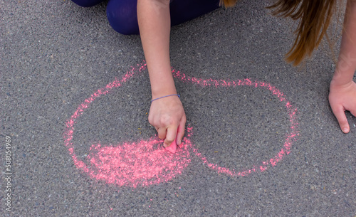 child's hand draws hearts, drawings chalk on asphalt