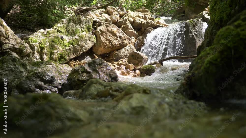 Low angle shot of small waterfall flowing between rocks in alp mountains during sunlight Low angle shot of small waterfall flowing between rocks in alp mountains during sunlight