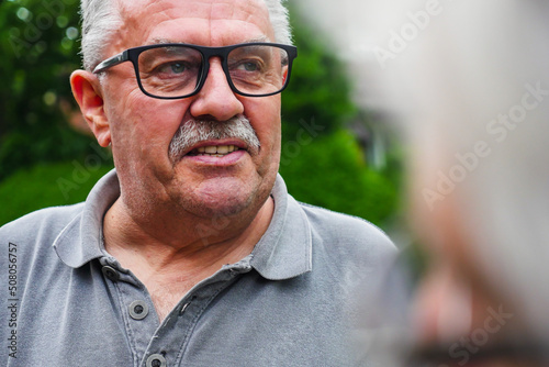 Elderly man with glasses standing outdoors looking away. Over the shoulder view.