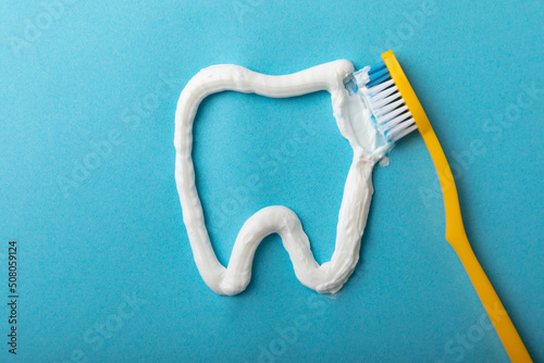 Tooth symbol made from toothpaste and a toothbrush on a blue background. Refreshing and whitening toothpaste. Copy space for text. Flat lay. Prevention of caries. The concept of teeth cleaning.