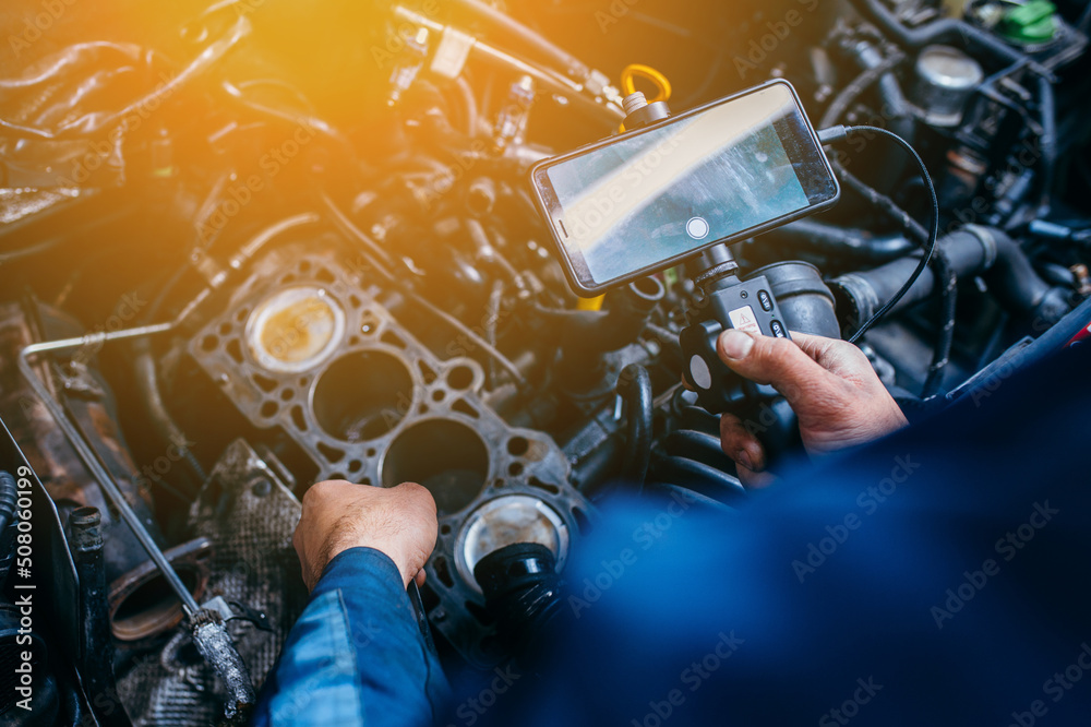 Hands of car mechanic check the vehicle engine with technical endoscope