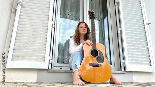 sad fair-haired girl sits with a guitar she thought she is dressed in a white blouse and blue jeans. High quality photo