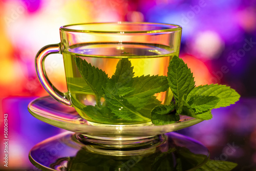 Cups of tea with fresh mint on multicolored background