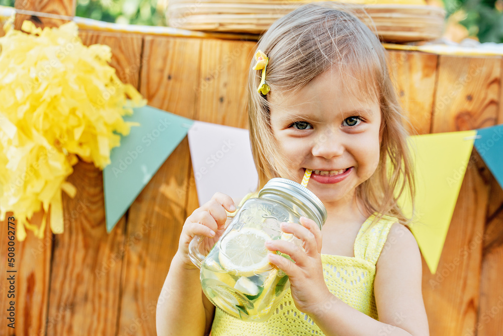 Foto de Child Girl drink natural lemonade at stand in park. Summer