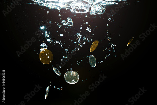 Close-up of money sinking in water. Treasure underwater. Gold and silver coins sink in the sea. Coins under water on a black background. Sinking money is a sign of a weak economy.